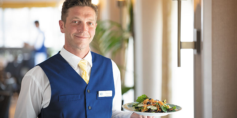 crew member smiling and holding up a plate of food