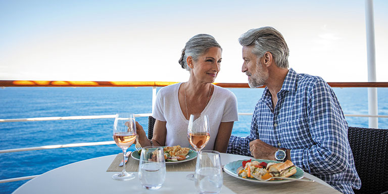 Mann und Frau genießen Essen und Wein an Deck eines Luxuskreuzfahrtschiffes mit Blick auf den Ozean