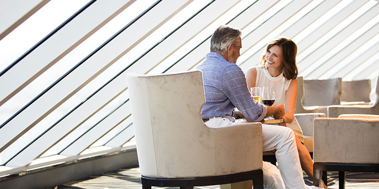 woman and man part of a cruise loyalty program smiling at each other enjoying alcoholic beverages