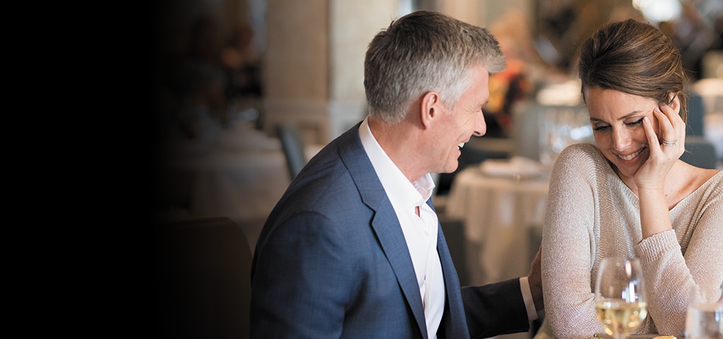 man and woman in nice clothes smiling at each other at table with white wine