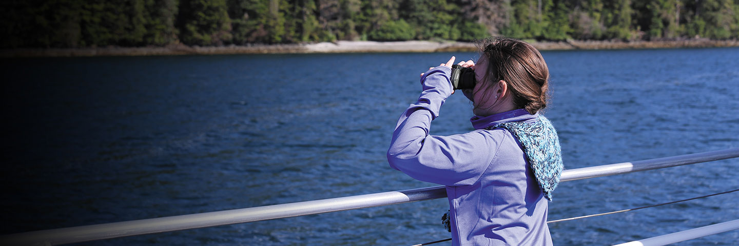 Ein junges Mädchen schaut an Deck eines Kreuzfahrtschiffes durch ein Fernglas