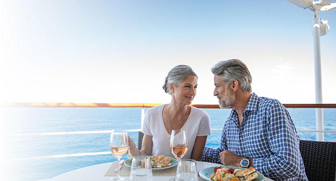 大海原を見晴らすラグジュアリーなクルーズ船のデッキで料理とワインを楽しむカップル