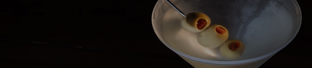 A classic dirty martini is served in a frosted cocktail glass against a dark, dramatic background