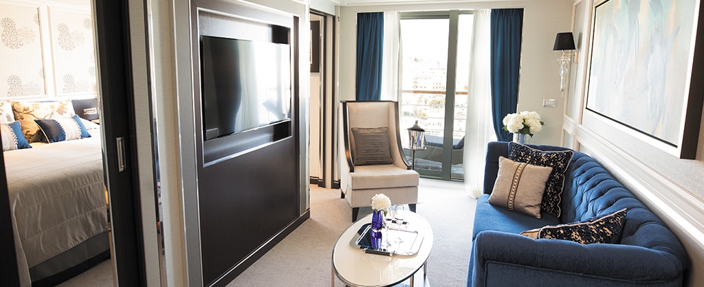 Geräumige Suite eines Kreuzfahrtschiffs mit blauer Deko und Blick auf den Balkon