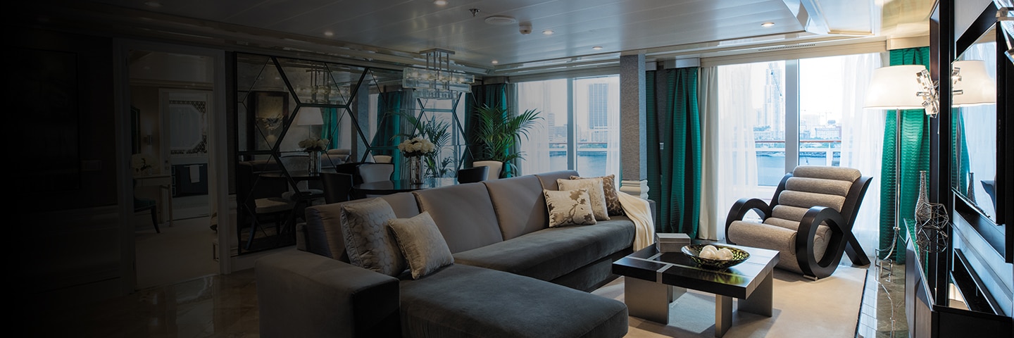 inside luxurious cruise suite living room with teal and gray decor and balcony