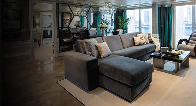 inside luxurious cruise suite living room with teal and gray decor and balcony