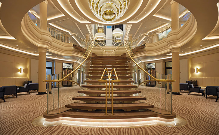 escalera de madera con un gran candelabro en el atrio del Seven Seas Splendor
