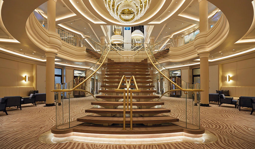 escalera de madera con un gran candelabro en el atrio del Seven Seas Splendor